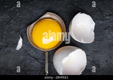 Hühnerdotter aus gebrochenem Bio-Ei in silbernem Löffel auf schwarzem Beton Hintergrund. Food-Fotografie Stockfoto