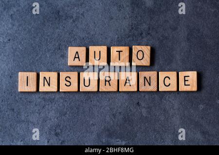 „Auto Insurance“ wurde in Holzfliesen auf dunklem, rauem Hintergrund geschrieben Stockfoto