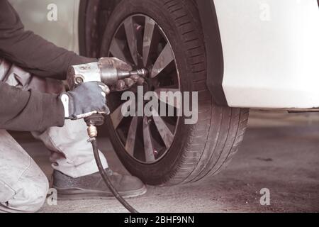 Das Rad mit einem pneumatischen Schraubendreher an das Auto Schrauben. Austausch von Saisonreifen in einer Autowerkstatt Stockfoto