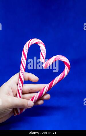 Liebe Weihnachtsferien. Kind hält zwei Süßigkeiten Sticks, bilden eine Herzform auf blauem Hintergrund. Konzentrieren Sie sich auf Candy Sticks und Hände.Copy Space.Candy Stockfoto