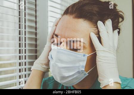 Die müde Krankenschwester schloss ihre Augen. Ein Arzt in einer chirurgischen Schutzmaske sieht nach einer geschäftigen Schicht im Krankenhaus während einer Coronavirus-Epidemie erschöpft aus. Stockfoto
