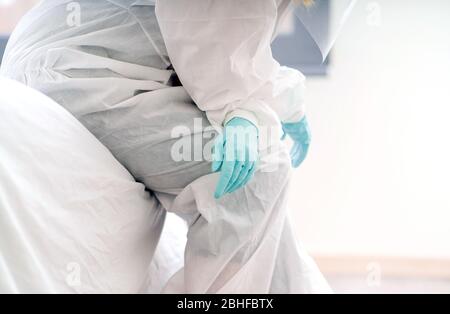 Detail eines Arztes, der im Krankenhauszimmer sitzt und einen Sicherheitsanzug und Latexschutzhandschuhe trägt Stockfoto