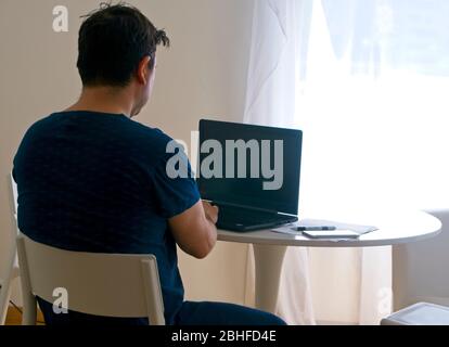 Junger Mann sitzt und arbeitet auf Laptop zu Hause. Konzept des Arbeitsvaters. Konzept der Telearbeit Stockfoto