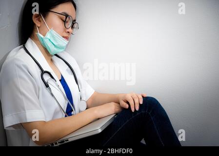 Asiatische junge Frau Arzt tragen Maske zur Sicherheit Coronavirus sitzen auf der Ecke Boden schlafen mit Erschöpfung von Überarbeit Konzept kümmern sich ist Stockfoto