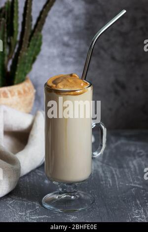 Dalgona Kaffee in einer transparenten Tasse mit einem Cocktail Stroh und Kaktus auf einem Betontisch. Stockfoto