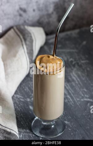Dalgona Kaffee in einer transparenten Tasse mit einem Cocktail Stroh auf einem Betontisch. Stockfoto