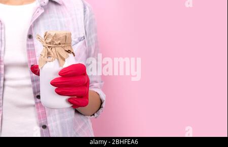 Frauen Hand in einem Gummihandschuh hält weiße Flasche auf rosa Hintergrund Stockfoto