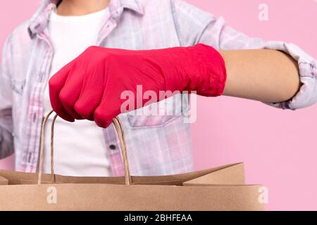 Frauen Hand in einem Gummihandschuh halten Papiertasche auf rosa Hintergrund Stockfoto