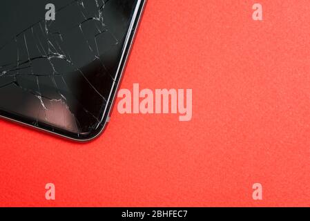 Handy mit Rissen auf rotem Hintergrund. Ein kaputtes Smartphone. Zerbrochenes Glas. Draufsicht, Kopierbereich Stockfoto