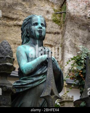 Alte Bronzestatue eines jungen Mädchens auf dem Petersplatz in Salzburg. Keine Menschen sichtbar, wolkige Tageslichtaufnahme. Felsen im Hintergrund. Stockfoto