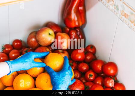 Indem Sie die sauberen und desinfizierten Früchte auf den Marmor in der Küche legen. Frau putzen Früchte, um Coronavirus mit blauen Latexhandschuhe zu verhindern Stockfoto