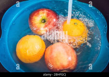 Blaue Schüssel mit Äpfeln und Orangen gefüllt mit Leitungswasser in der Spüle. Desinfektion der Früchte, um die Ausbreitung des Coronavirus zu verhindern. Stockfoto