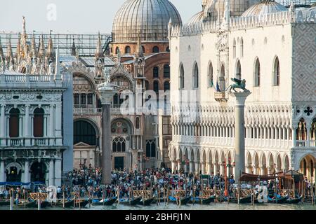 Menschenmassen versammeln sich auf dem Markusplatz. - Markusplatz in der Nähe der Gondelanlegestelle auf dem Canal Grande. Venedig, Italien. Schatten am späten Nachmittag. Stockfoto