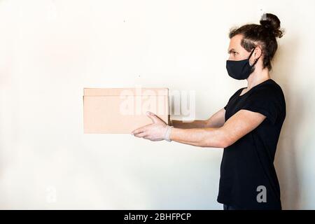 Liefermann, der Pappkartons in medizinischen Handschuhen und Schutzmaske gibt. Online-Shopping und Express-Lieferung während der Quarantäne Stockfoto