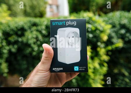Paris, Frankreich - 1. August 2019: Männliche Hand-Paket mit Amazon neuen Smart-Stecker Arbeit mit Alexa Personal Assistant - grüne Natur Hintergrund Stockfoto