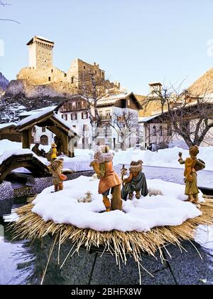 Ossana, Italien - 26. Dezember 2019: Krippe im Freien im Schnee bedeckt. Im Hintergrund die berühmte Burg von San Michele. Stockfoto