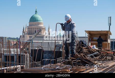 23. April 2020, Brandenburg, Potsdam: Auf dem Dach des Grundbaues der Garnisonskirche arbeitet ein Stahl- und Betonbauer an der Bewehrung für den Betonguss. Im Hintergrund sieht man die Kuppel der Kirche St. Nikolai. Im Inneren des rund 17 Meter hohen Sockelgebäudes soll auf zwei Etagen eine Kapelle errichtet werden, neben einem Café, einem großen Ausstellungsraum und Seminarräumen. Der Umbau des Turms der ehemaligen Militärkirche soll bis Sommer 2022 abgeschlossen sein. Die Kirche wurde zwischen 1730 und 1735 nach den Plänen des Architekten gebaut Stockfoto