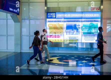 Reisende gehen am Dallas/Fort Worth International Airport an einem Warnschild für COVID-19/Coronavirus-Symptome vorbei. Da Covid-19 weiter verbreitet wird und die Länder mit Reiseverboten und Reiseberatungen reagieren, ist die weltweite Nachfrage nach Flügen gesunken. Infolgedessen sind Fluggesellschaften gezwungen worden, Strecken mit einigen nahezu leeren Flugzeugen zu kürzen. Viele Fluggesellschaften bieten ihren Kunden jetzt die Möglichkeit, Flüge kostenlos zu ändern oder zu stornieren. Stockfoto