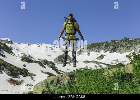 Mann Reisende mit Sportbekleidung und Rucksack in der Luft schwebt ausgestattet, während vor dem Hintergrund von schneebedeckten Felsen und blauen Himmel springen. Konzept der Freude Stockfoto