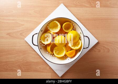 High-Angle-Aufnahme eines Collnders mit Zitronenhälften gefüllt Reste von der Herstellung von hausgemachten Limonade, auf einem Holztisch und weißen Marmorfliesen. Stockfoto