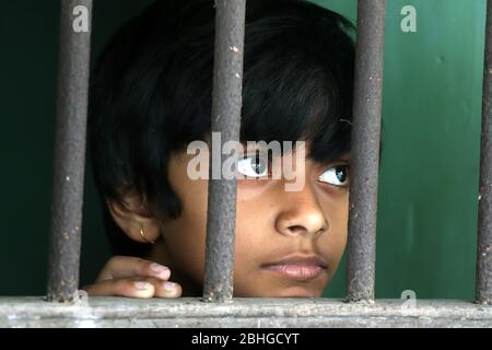 Porträt eines traurigen unschuldigen Kindes, das aus dem Fenster schaut. Trauriges Mädchen schaut nachdenklich durch das Fenster zu Hause. Kleines Mädchen gezwungen, zu Hause zu bleiben Stockfoto