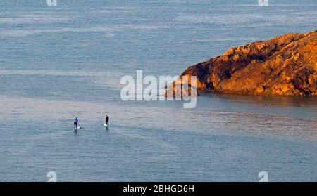 Langland Bay, Swansea, Großbritannien. April 2020. Das frühe Morgenlicht fällt auf Snaple Point in Langland Bay in der Nähe von Swansea, während ein Paar Stand Up Paddlebarder heute bei sonnigem Wetter aufs Meer aufbrechen. Kredit: Phil Rees/Alamy Live News Stockfoto