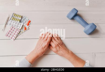 Ältere Hände mit Pillen, Medikamente auf dem Tisch, Glocke. Frau runzelte Hände, Thermometer, bunte Tabletten und stumpfe Glocke, Holzhintergrund. Gesundheitswesen Stockfoto