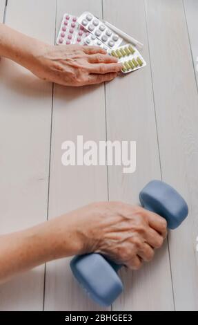 Ältere Hände mit Pillen, Medikamente auf dem Tisch, Glocke. Frau runzelte Hände, Thermometer, bunte Tabletten und stumpfe Glocke, Holzhintergrund. Gesundheitswesen Stockfoto