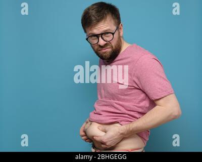 Der verärgerte Mann zeigt und hält mit den Händen sein überschüssiges Fett auf dem Bauch. Kopierbereich. Übergewichtige Person. Gesundes Lifestyle-Konzept. Stockfoto