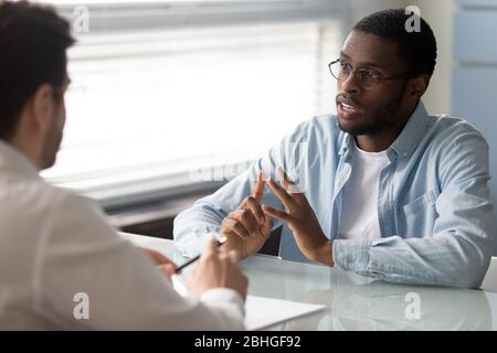 Seriöse afroamerikanische Kandidat im Gespräch mit Geschäftsmann bei Vorstellungsgespräch. Stockfoto