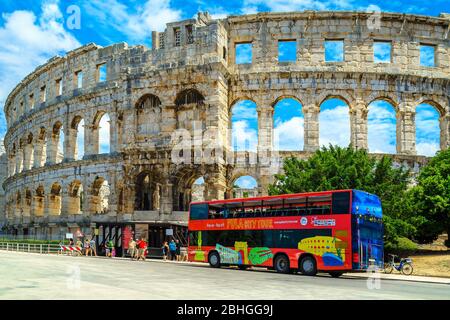 PULA, KROATIEN - 15. JUNI 2015: Beliebtes Reiseziel mit dem berühmten römischen Amphitheater (Arena) Gebäude. Bunte Sightseeing-Bus mit Touristen i