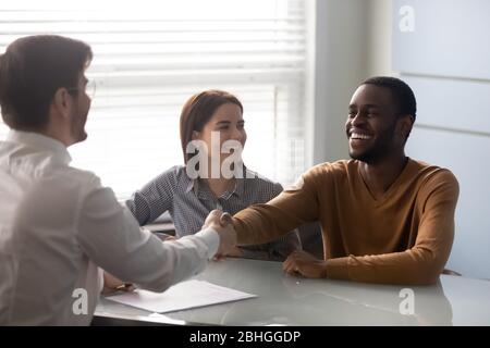 Lächelnder afroamerikanischer Ehemann, der die Hände mit Geschäftsmann schüttelt. Stockfoto