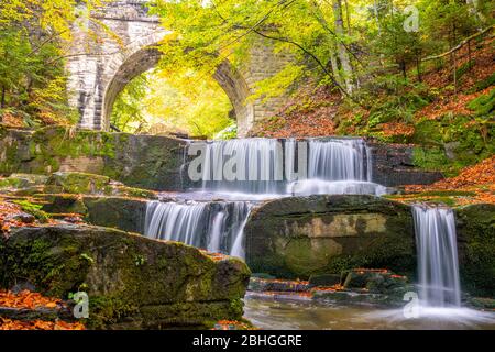 Sommertag im sonnigen Wald. Alte Steinbrücke. Kleiner Fluss und mehrere natürliche Wasserfälle Stockfoto