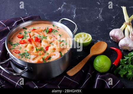 Nahaufnahme von Tom Yum Suppe, tom Kha Suppe in einem Topf auf einem Betontisch mit braunem Tuch und Löffel, horizontale Ansicht von oben, Stockfoto