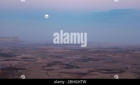 Vollmond blickt durch Wolken über dem makhtesh ramon Krater in israel kurz nach Sonnenuntergang in mitzpe ramon in israel Stockfoto