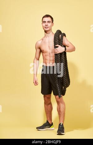 Junge Athlet mit Teppich und Seil im Studio auf gelbem Hintergrund Stockfoto
