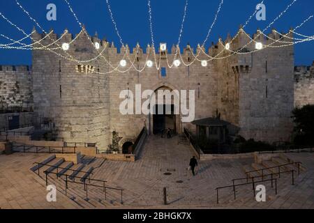 Jerusalem, Israel. April 2020. Ein einiger Fußgänger betritt das Nablus-Tor, das auch Damaskus-Tor genannt wird, das während des muslimischen heiligen Monats Ramadan inmitten der COVID-19-Pandemie mit festlichen Lichtern geschmückt ist. Alte Stadt Jerusalem, Israel. Stockfoto