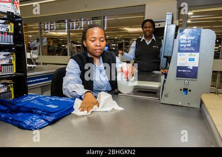 Kapstadt, Südafrika - 23. März 2020: Kassenpersonal an der Kasse wischt während des Virus-Ausbruchs Oberflächen im Pick 'n Pay-Lebensmittelgeschäft ab Stockfoto