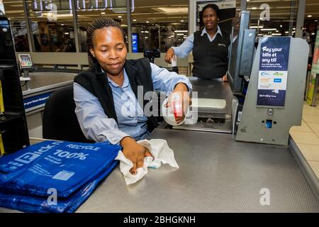 Kapstadt, Südafrika - 23. März 2020: Kassenpersonal an der Kasse wischt während des Virus-Ausbruchs Oberflächen im Pick 'n Pay-Lebensmittelgeschäft ab Stockfoto