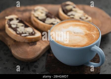 Frischer Cappuccino in blauer Tasse mit Toasts mit Schokoladenaufstrich Auf konkretem Hintergrund Stockfoto