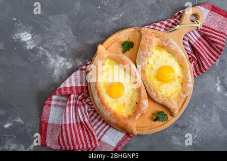 Khachapuri in Adjarian. Traditionelle georgische und armenische Küche. Offener Kuchen mit Suluguni-Käse und Eigelb in Form eines Bootes auf einem Holzbrett. Stockfoto