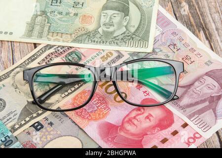 Augengläser mit internationalen Weltbanknoten variieren Länderhintergrund. US-Dollar, chinesischer Yuan, japanischer Yen, Euro, Korea gewonnen, Thai Baht. Konzept o Stockfoto