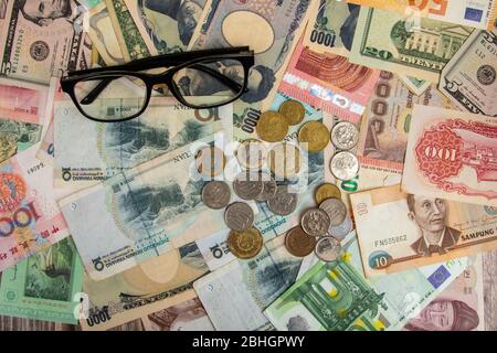 Augengläser mit internationalen Weltbanknoten variieren Länderhintergrund. US-Dollar, chinesischer Yuan, japanischer Yen, Euro, Korea gewonnen, Thai Baht. Konzept o Stockfoto