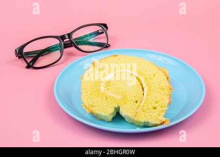 Brillen Brille und Slice of Swiss Rolle auf rosa Hintergrund. Konzept Für Eine Teepause Stockfoto