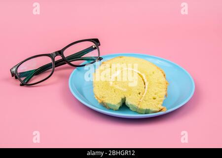 Brillen Brille und Slice of Swiss Rolle auf rosa Hintergrund. Konzept Für Eine Teepause Stockfoto