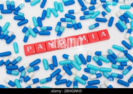 Verstreute blaue Pillen Caplets und roten Buchstaben Fliesen: PANDÄMIE - Spanisch, Italienisch & Polnisch Substantiv für Pandemie. Coronavirus conceptual, Covid 19 Metapher. Stockfoto