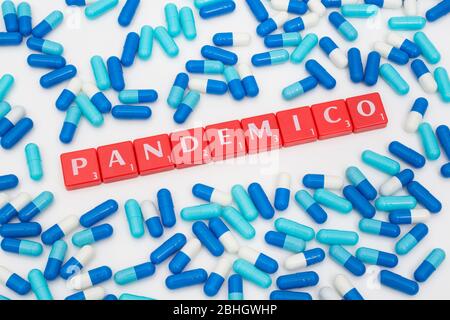 Verstreute blaue Pillen Kaplets und rote Buchstaben Fliesen: PANDEMICO - Spanisch & Italienisch Adjektiv für Pandemie. Coronavirus conceptual, Covid 19 Metapher. Stockfoto