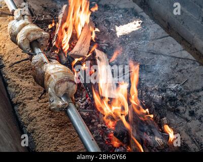 Auf Spieß gebratenes Huhn, das über den leuchtend glühenden Buchenholzkohlen gegrillt wird. Ganze Hühner mit Gewürzbürste auf Grill drehen. Stockfoto