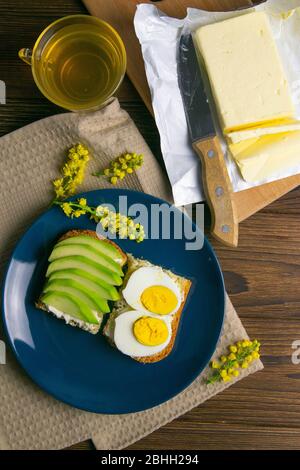 Sandwich mit Avocado und pochiertem Ei auf blauem Teller auf Holztisch Stockfoto