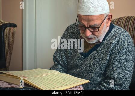 Ankara/Türkei - 24.04.2020: Sehr alter türkischer muslim mit Gebetsmütze, der das heiligste Buch, den Koran, im Ramadan-Monat rezitiert Stockfoto